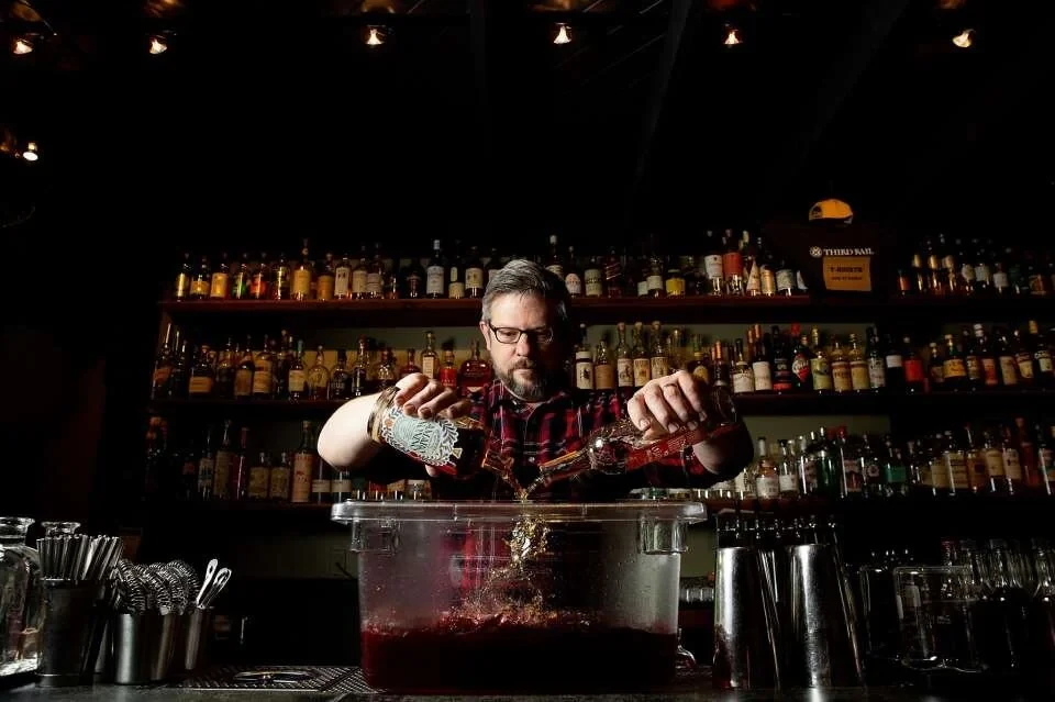 Jeff Lyon pours two bottles into a large punch container behind the bar at Third Rail.