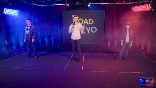 Three artists wearing VR headsets compete on a stage lit in blue and red, with Road to Tokyo projected behind them.
