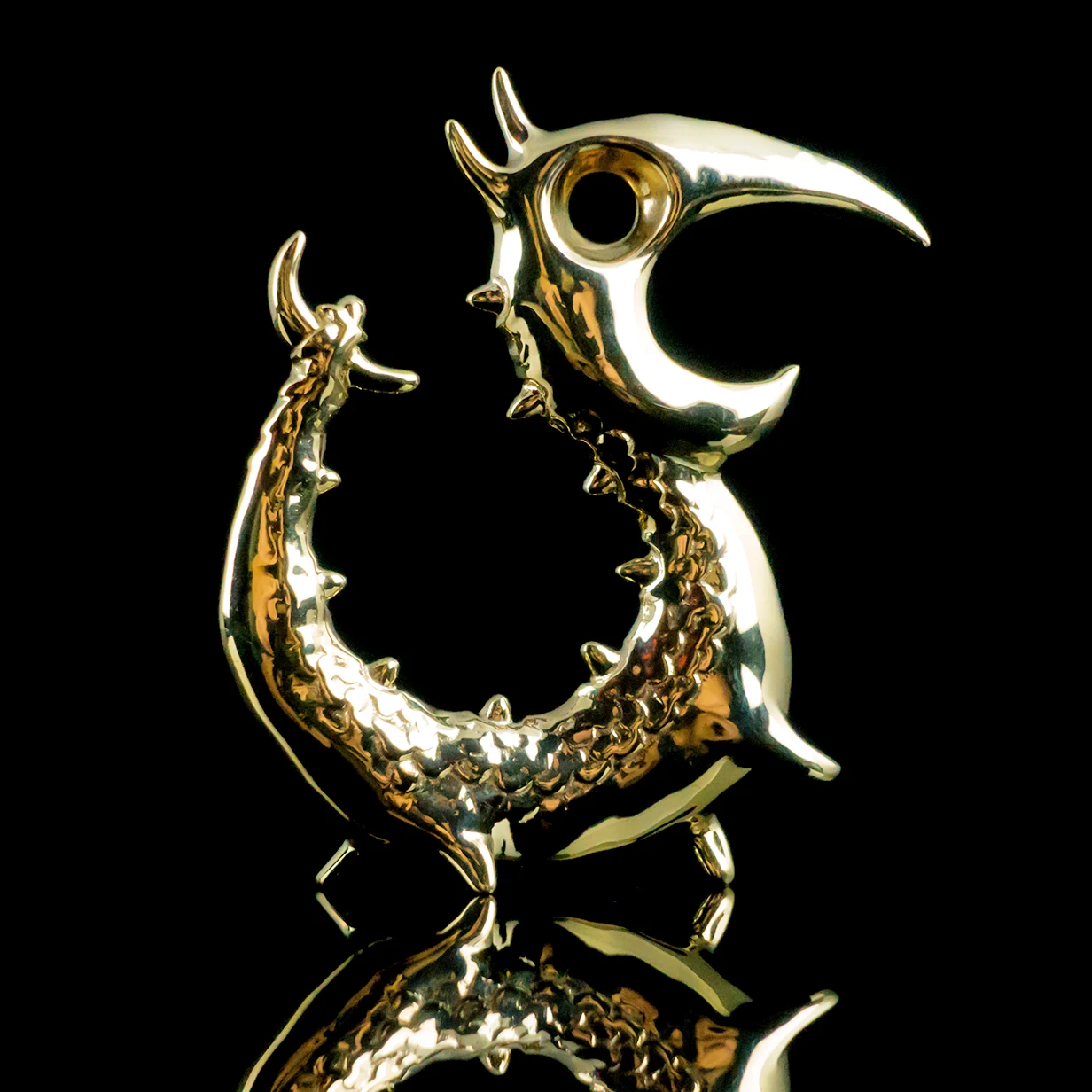 Polished lost-wax brass Dragon Opener reflected against a black background.