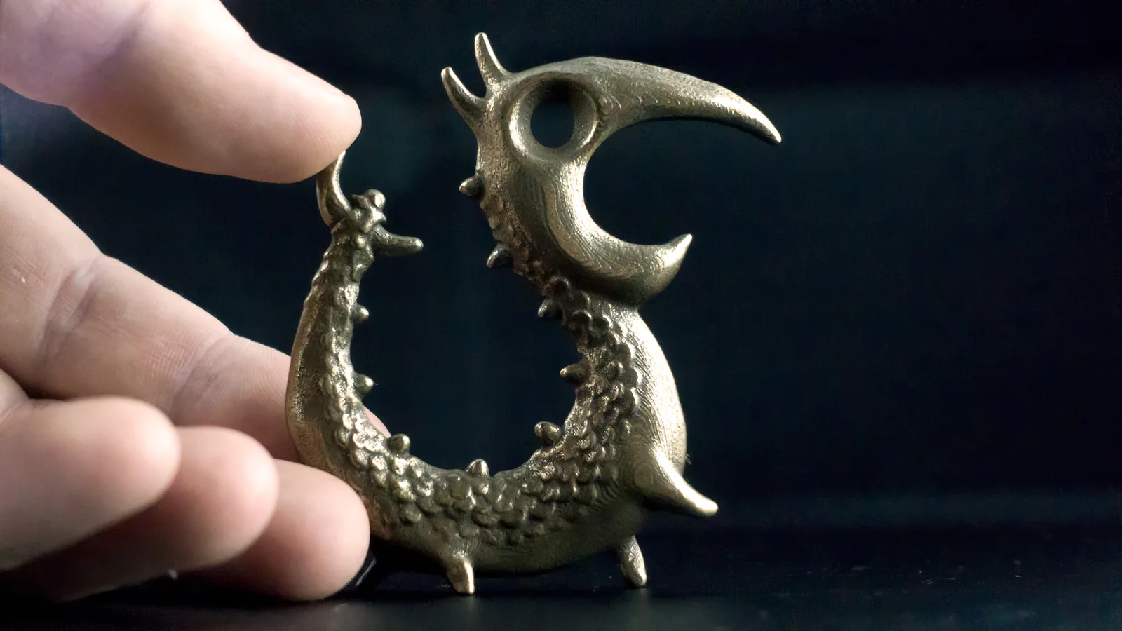 The hollow 2017 steel Dragon Opener prototype held between Dylan's fingers.