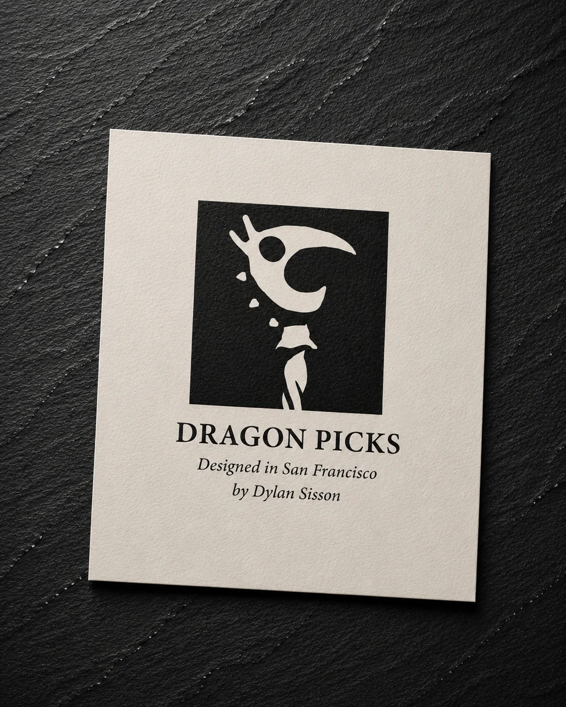 Open Dragon Picks sample box with four chrome picks in a black fitted insert and a printed card beside it.