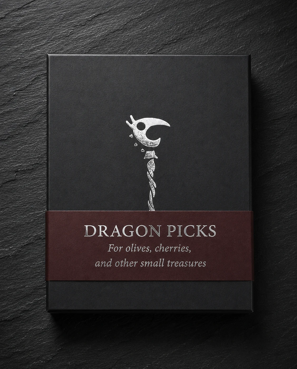 The closed matte-black Dragon Picks box with its burgundy paper wrap and silver dragon mark.