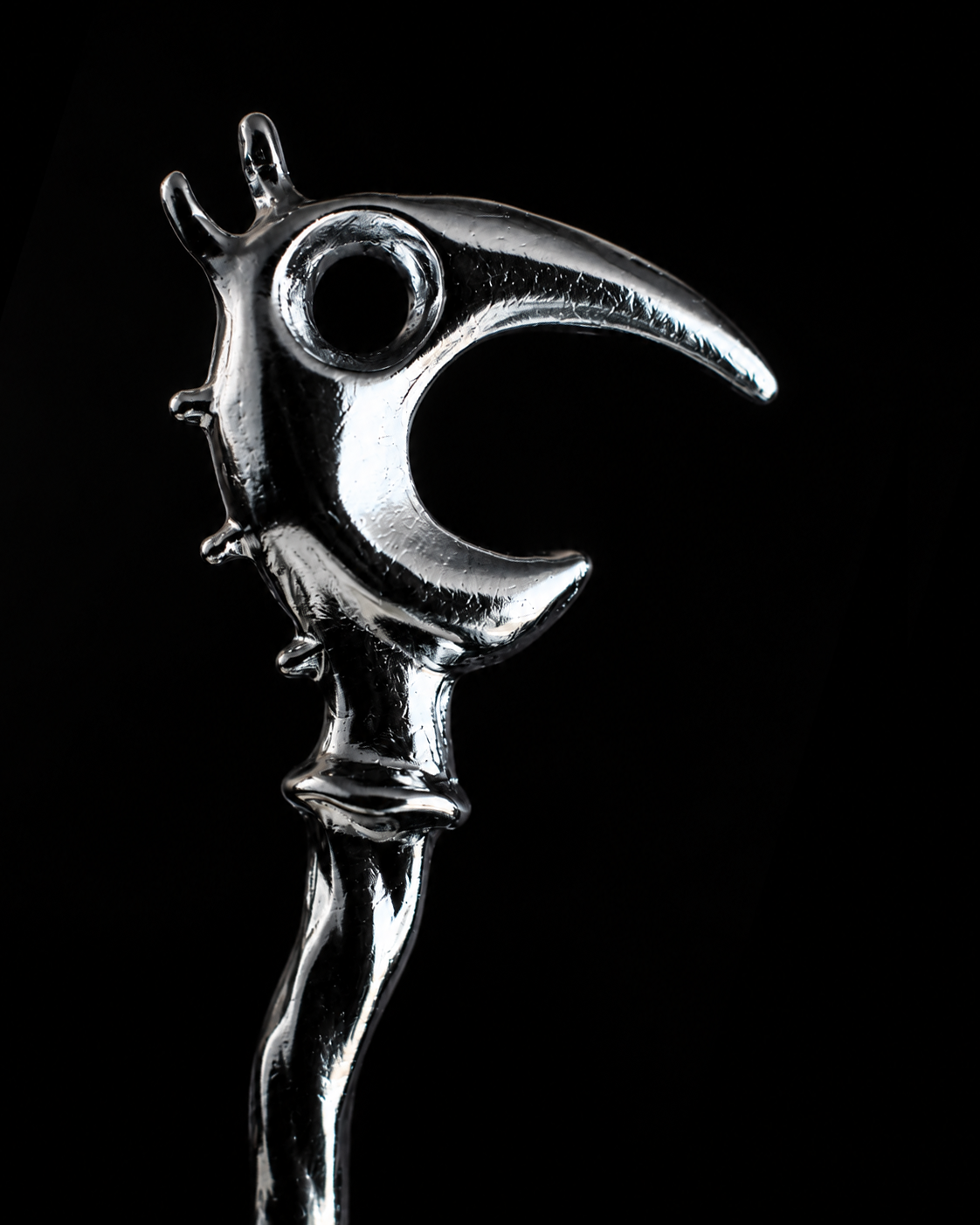 Polished silver Dragon Pick rising from a field of black negative space.