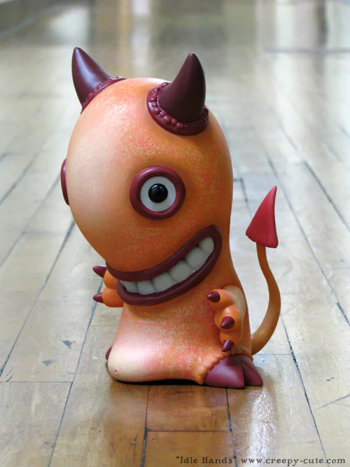 The orange Idle Hands vinyl figure posed alone on a polished wood floor.