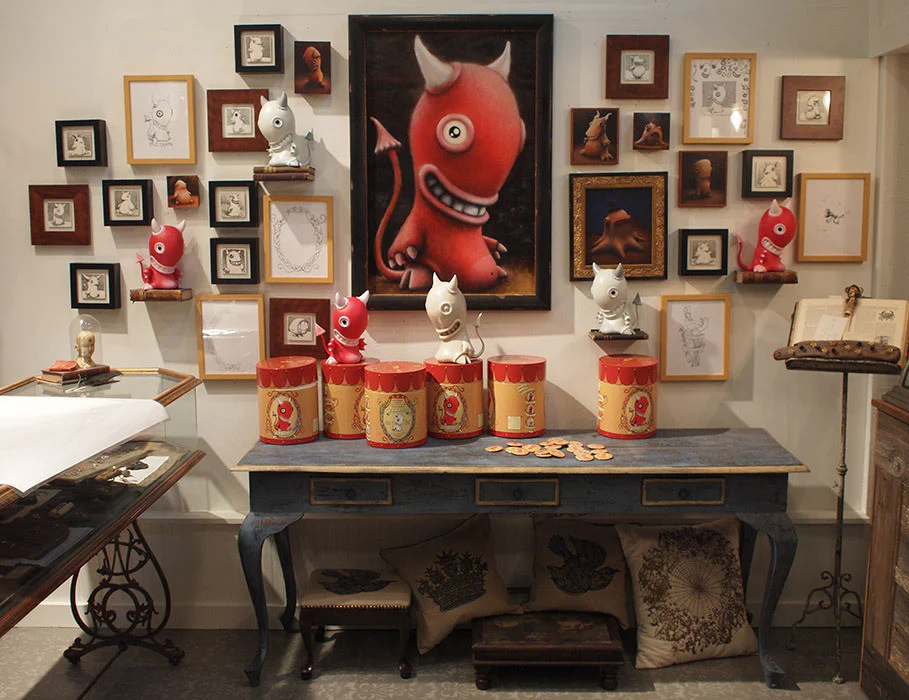 A gallery installation filled with Idle Hands paintings, drawings, all three vinyl toy colorways, cylindrical packages, and coasters.