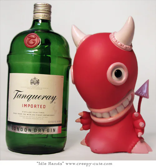 The pink Idle Hands vinyl figure standing beside a large green gin bottle.