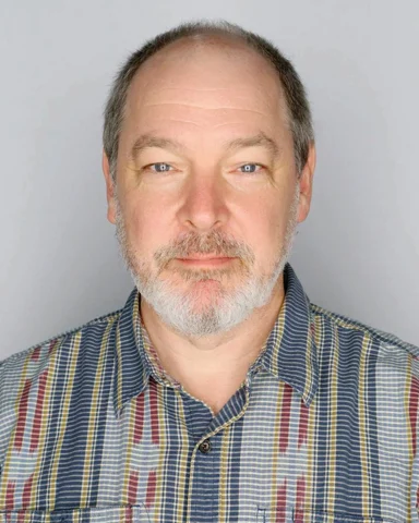 Dylan Sisson facing the camera in a checked shirt against a light gray background.
