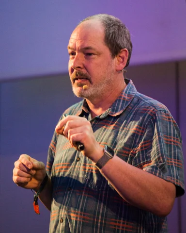 Close-up of Dylan Sisson presenting with a headset microphone and handheld clicker.