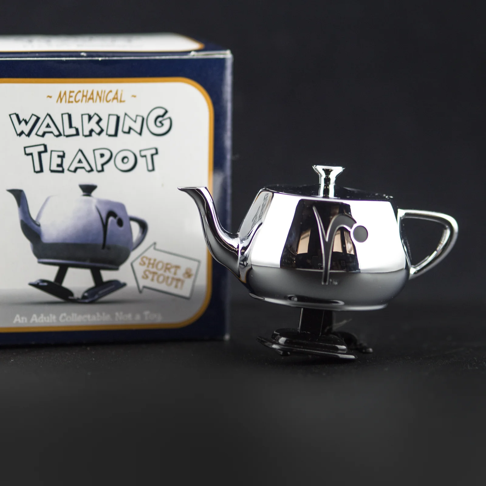 The original silver RenderMan Walking Teapot standing beside its illustrated box.