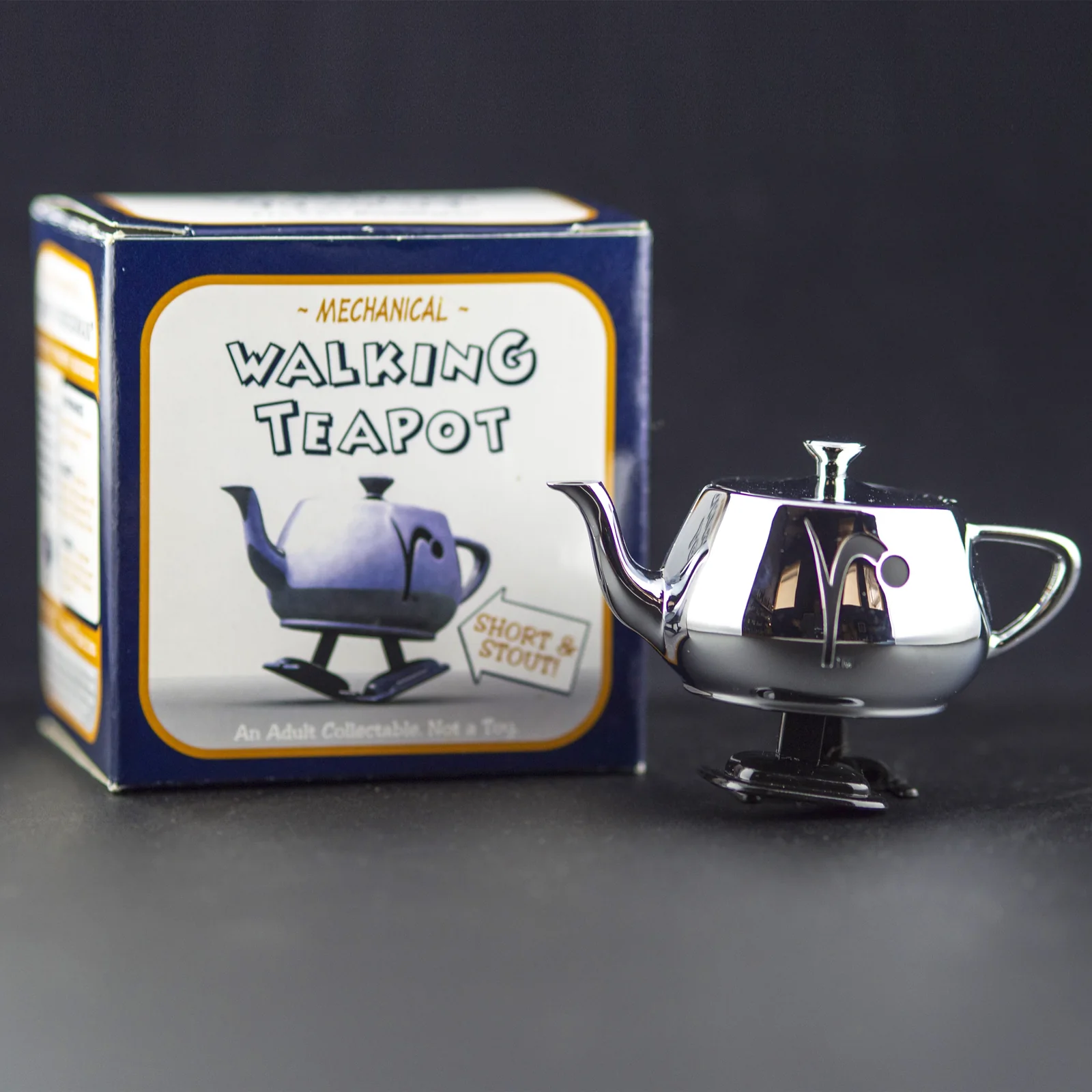 The polished silver 2003 RenderMan Walking Teapot standing beside its navy Mechanical Walking Teapot box.